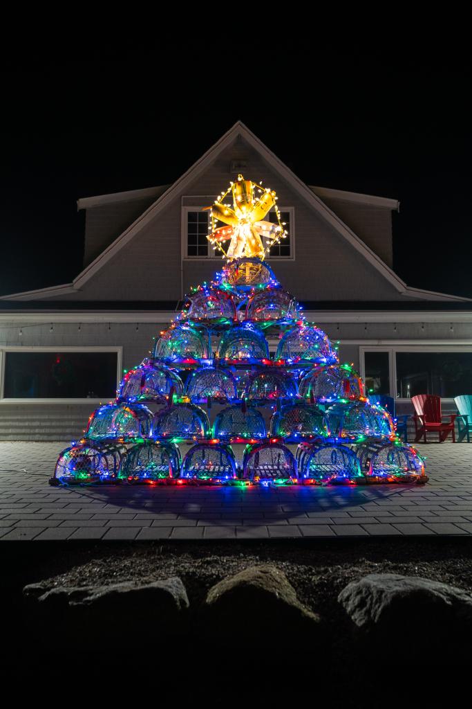 wooden lobster traps are stacked and decorated with lights to look like a christmas tree shape. a large yellow star is on top