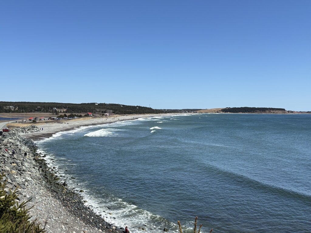 View of Lawrencetown Beach along Nova Scotia’s Eastern Shore, with gentle waves rolling toward a rocky and sandy coastline dotted with small buildings.
