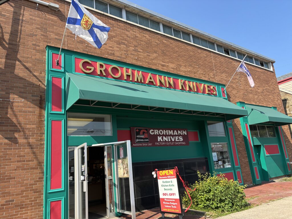 Exterior of Grohmann Knives in Pictou, a local factory outlet known for handmade knives, with bold green and red trim and Nova Scotia flags above the door.