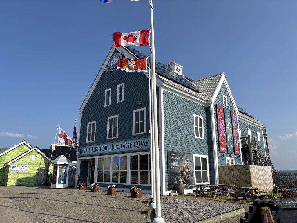The Hector Heritage Quay in Pictou, Nova Scotia, a blue historic building with Canadian flags and vibrant banners, honours Scottish immigration history.