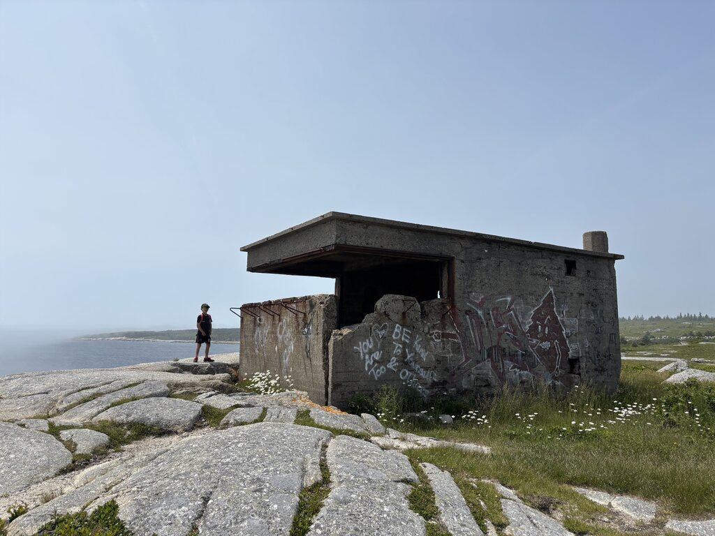 A child stands near a graffiti-covered concrete bunker overlooking the ocean at the end of the Duncan’s Cove hiking trail in Nova Scotia. The rugged granite landscape and moody sky add to the remote, windswept feel of the scene.
